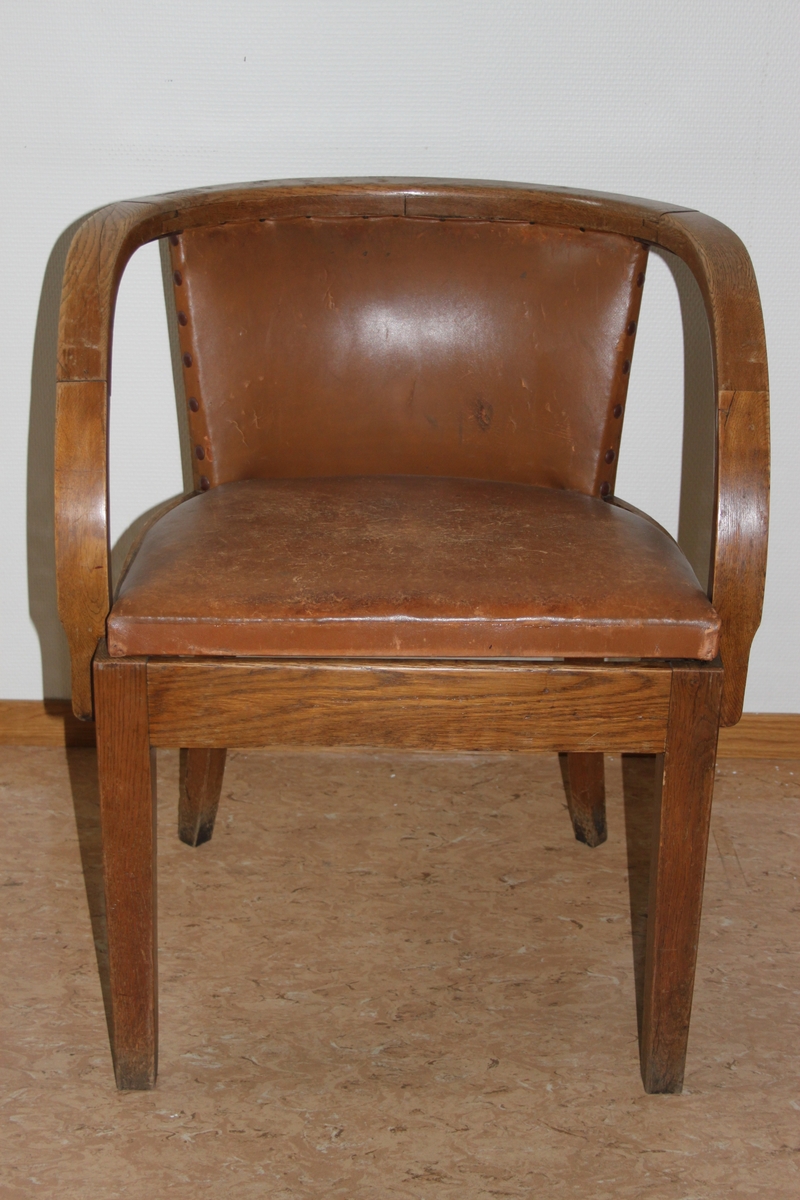 Møteromstol/kontorstol med armlener samt buet rygg. 4 ben. Metallbeslag under armlener. Brunt skinn i rygg og sete. Stolen er lakket med klar lakk. Originalt møbel innkjøpt til det nye Statsarkivet i Kristiansand i 1935.