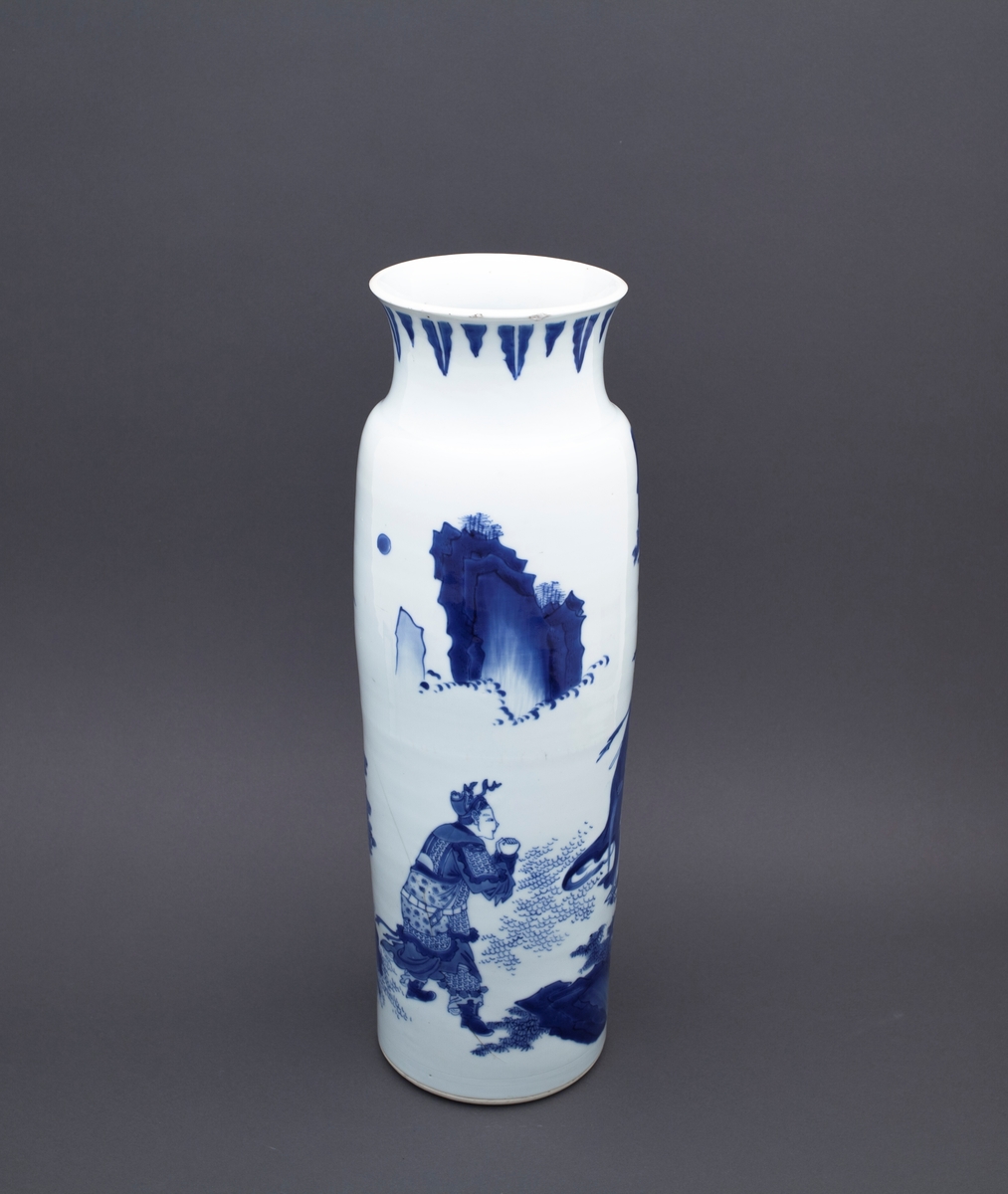 Tre mennesker står foran et stort tre. I bakgrunnen ser vi to fjelltopper. En mann står med foldete hender foran en annen mannsfigur. Han har skjegg, et sverd på ryggen og han holder i en vifte. Ved siden av mannsfiguren med sverd og vifte finner vi en kvinneskikkelse, som også holder i en vifte.