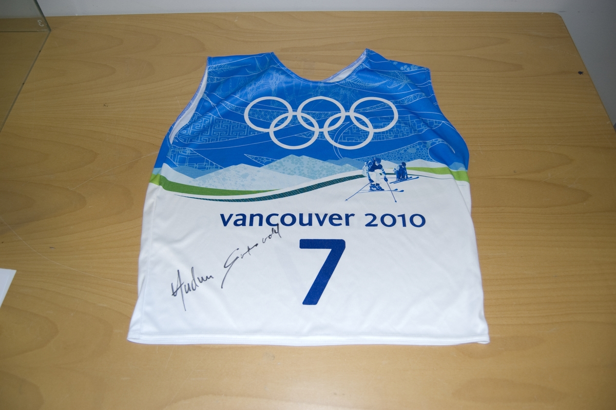 Flerfarget startnummer med nr. 7. På nummeret er det motiv av de olympiske ringene og to skicrosskjørere. Nummeret er signert.