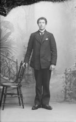 Portrett, mann står ved stol, helfigur