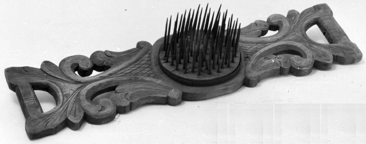 Hekle av tre med akantusutskjæringer. På midten av brettet er det en avrundet form med snålnagler.