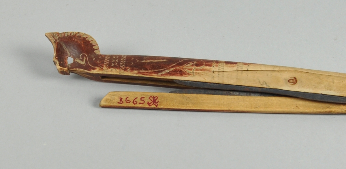 En trestav som er uthulet i den ene enden, og i uthulingen er det montert en mindre trestav. Begge stavene har påmontert en knivegg av messing. Staven er dekorert med utskjæringer av linblad, og enden på trestaven er skåret ut som et hestehode.