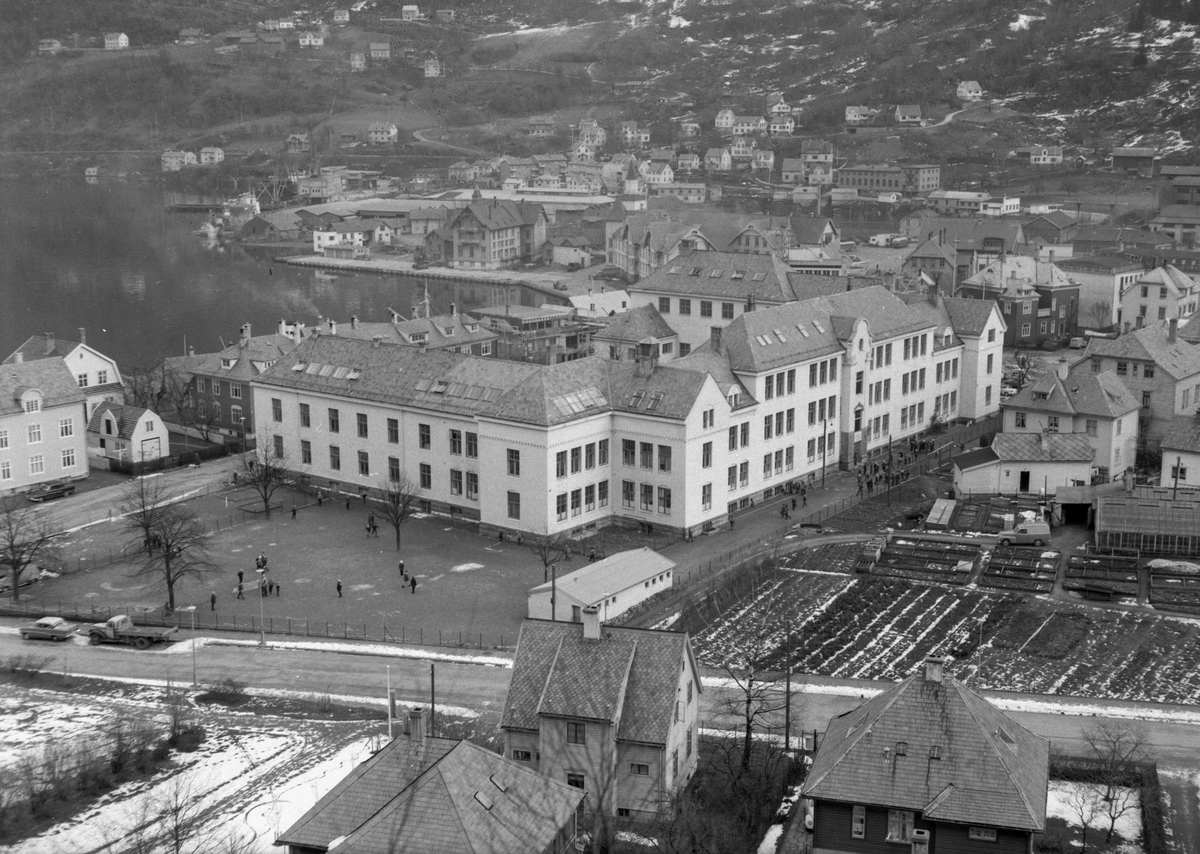 Oversikt Odda sentrum, Odda barneskule, elev  på leikeplassen, Breisteins gartneri, Opheimsgata, apotek, Grand Hotell, Freim og Ragde i bakgrunnen,
Odda Meieri, lastebil, bil