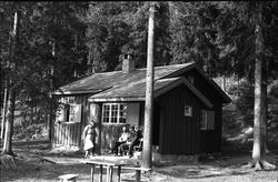 Tre personer ved ei hytt,e trolig på Totenåsen. Fra venstre: