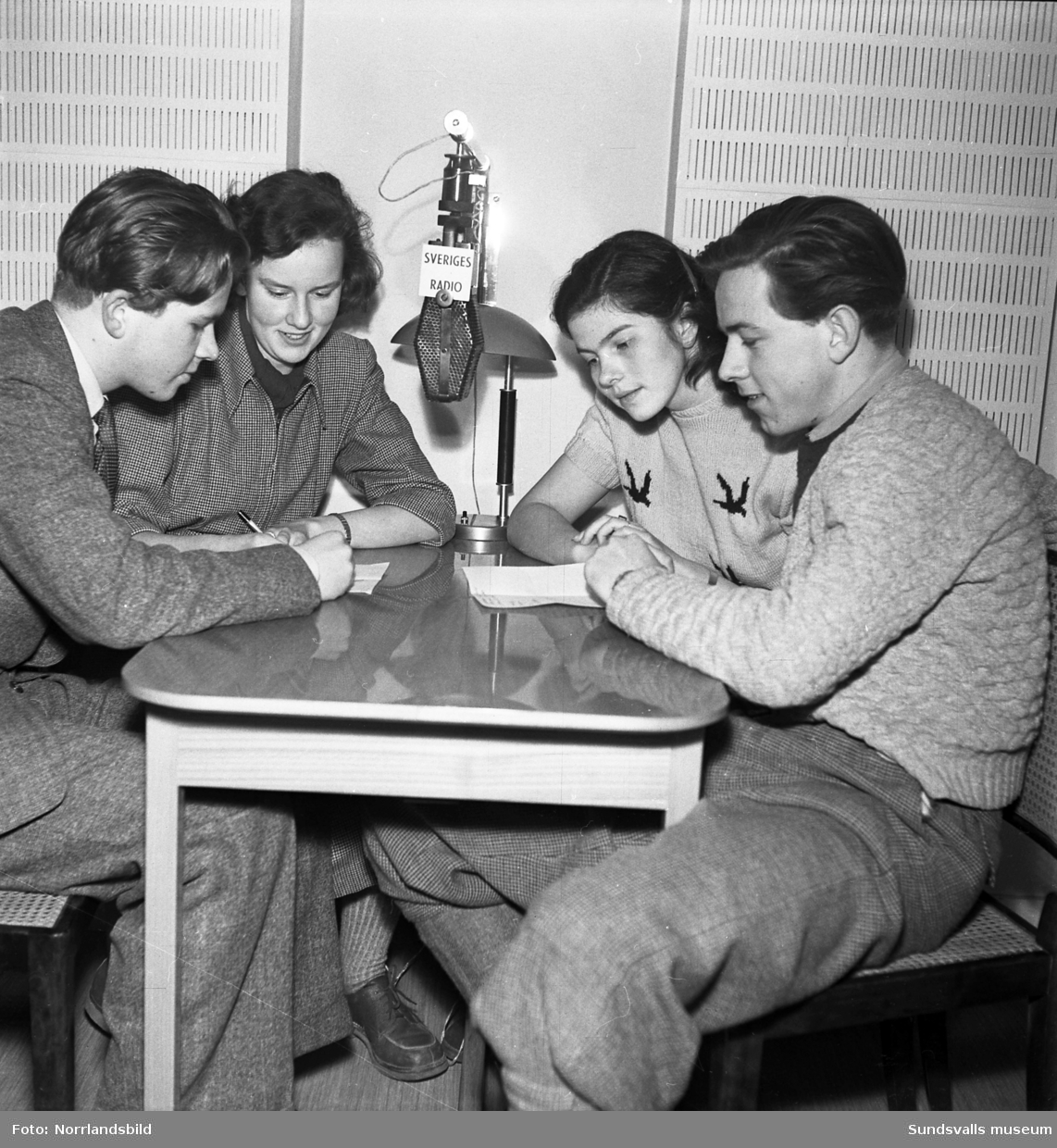 Inspelning av ett radioprogram, frågesport mellan Sundsvall och Stockholm. Fyra ungdomar koncentrerar sig runt mikrofonen.