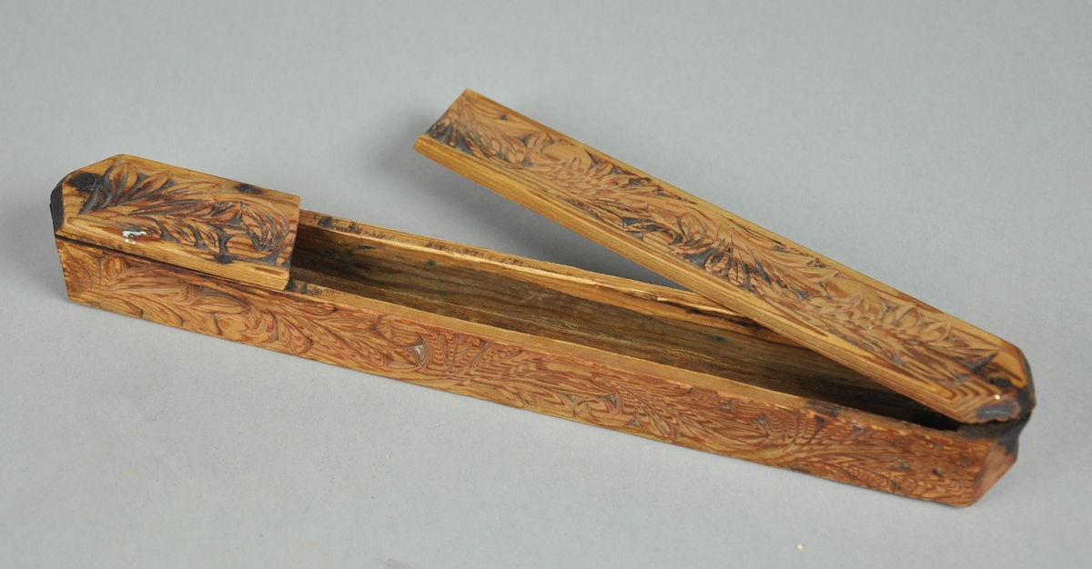 Pennal av tre med akantusutskjæringer på tre sider. Pennalet har et lokk som kan skyves til siden og er festet med en spiker.