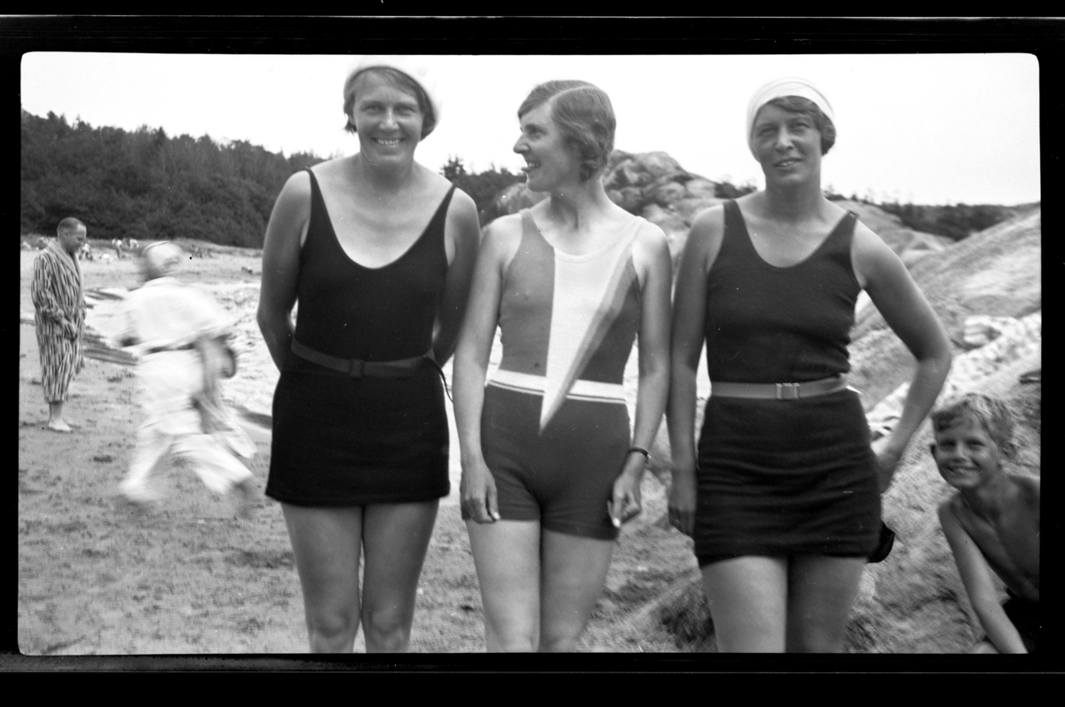 Tre søstre i badedrakt på stranden på Ula i Vestfold. Fra venstre Betsy Hansen, Hilda Sundt og Lillly Moestue. Rolf Sundt Jr. titter frem fra høyre.  Fotografert 1932.
