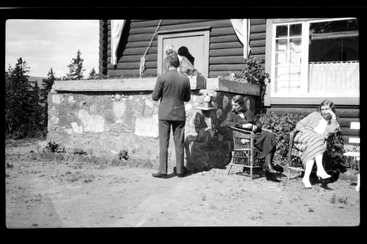 Johan Buratti med ryggen til,  hans hustru Agnes Buratti og Hilda Sundt sitter foran en stor hytta. Fotografert 1928.