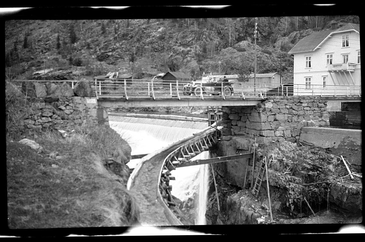 En bli står på broen, en tømmerrenne blir ført ut fra en foss under en broen. Fotografert 1926.
