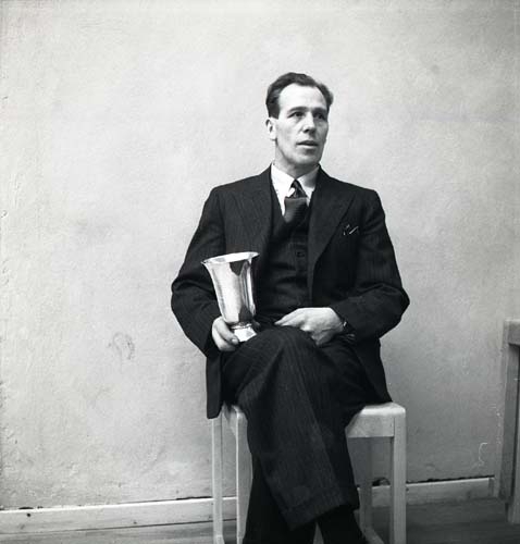 En man iklädd kostym sitter på en stol med en prispokal i handen. Unga Odlare, 1948.