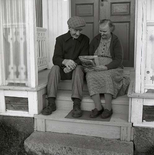Ett äldre par sitter ute på förstukvisten och läser i en tidning, Änga, Arbrå 1964.
