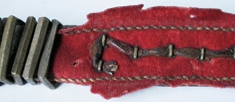 Ett par knäbälten av läder med rött kläde på undersidan och med synlig kant på ovansidan. Spännen, tännikor och beslag av mässing.