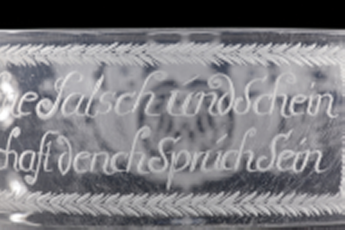 Skål av glas med hänklar. 
Graverad dekor med två spegelmonogram under friherrekronor och tysk text: "Treu Redlich ohne Falsch und Schein, Soll unser FreundSchaft dench Spruch Sein". 
Vilar på tre kulfötter.