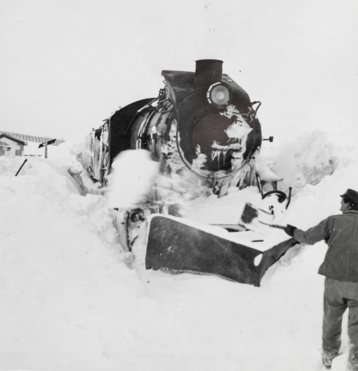 Toget fra Mo i Rana til Lønsdal har kjørt seg fast i snøen på Saltfjellet. Jernbanepersonalet arbeider med å spa løs toget. Damplokomotiv type 33c nr. 396.