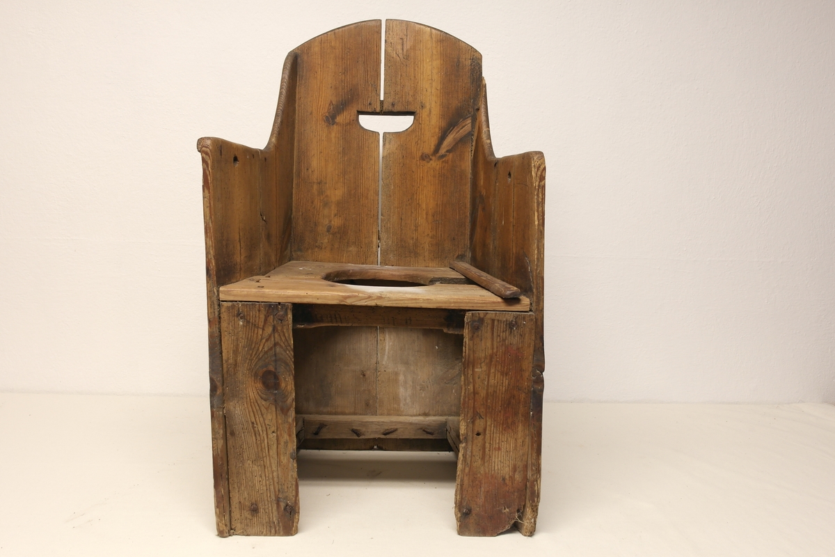 Dostol i tre. Stolen har en utsparing i ryggen (bærehåndtak) og åpning foran for potte/kar. Stolen har vært malt rød. Inngravert initialer og årstall bak på stolryggen.