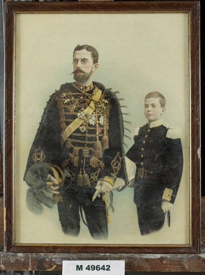 Oljetryck.
Dubbelporträtt (efter foto) föreställande dåv. kronprins Gustaf (V) och hans son,  dåv. arvprins Gustaf Adolf 
(blivande Gustaf VI Adolf). 
Båda är klädda i uniform.