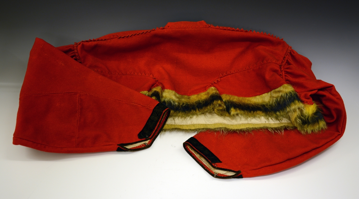 Fra protokollen: Rød brudetrøyi. silkesømmet i flammesym,fra aarene 1850-60. Trøyen av rødt klæde, med gul, uldhaarsvevet kantning nede. Sømmene forsirede med klædesfrynser i triangulære tunger. Omslagstrøye med hægter foran; 2 rynker nederst paa rygstykket. Armene kantede med grønne fløyielsborder.