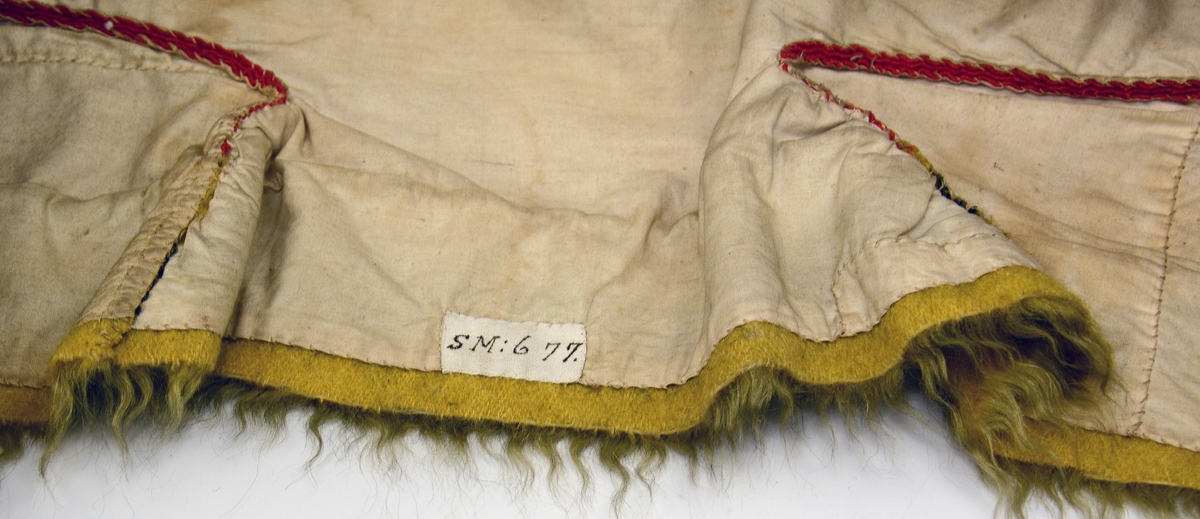 Fra protokollen: Rød brudetrøyi. silkesømmet i flammesym,fra aarene 1850-60. Trøyen av rødt klæde, med gul, uldhaarsvevet kantning nede. Sømmene forsirede med klædesfrynser i triangulære tunger. Omslagstrøye med hægter foran; 2 rynker nederst paa rygstykket. Armene kantede med grønne fløyielsborder.