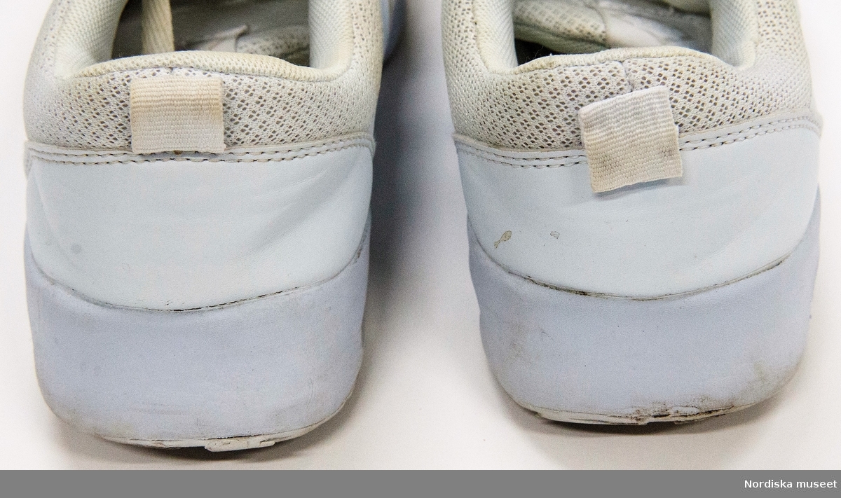 Ett par vita sneakers. Sula av plast (phylon och TPR=ThermoPlastic Rubber) med transparent plastbit under i hälen. Överdel av syntettyg och läderimitation. Snörning med vita platta skosnören genom sju par hål. Plös. Insida av syntettyg. Liten bandögla på bakkappan. 
På plösen etikett med text: 
"157 SOULS
STYLE: O2/A Shoe
SIZE: EU 45
SIZE: EU 11
MADE IN CHINA"
På innersulan svart text: "...157 SOULS".

Anmärkning: text delvis bortnött på innersulan. Bruna fläckar på ovansidans främre del.
/Leif Wallin 2017-06-07