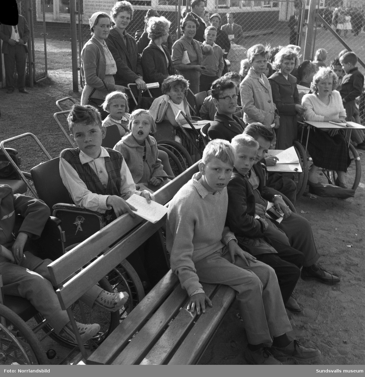 En grupp barn från Vanföreanstalten i Härnösand besöker Bergsåkers travbana, ett populärt utflyktsmål enligt reportaget i Dagbladet 1959. Tre av de som är med på bilden är: Gerd Söderberg, Sven Hellström och Emmy Tieusonen.