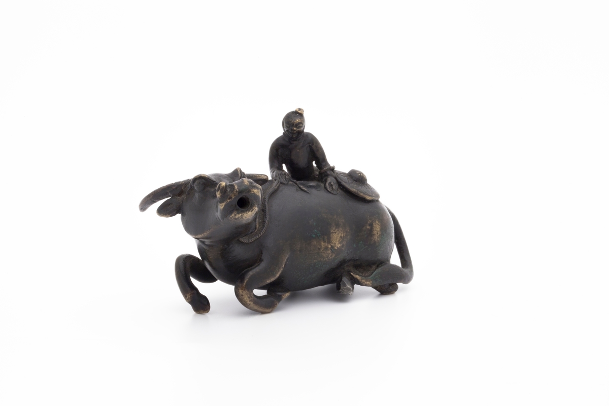 Vanndrypperen forestiller en mannsfigur som bestiger en vannbøffel. Han holder tauet festet til bøffelens mule i den ene hånden mens han løfter seg opp med den andre. Bak på ryggen ligger hatten hans, som er rikt dekorert.