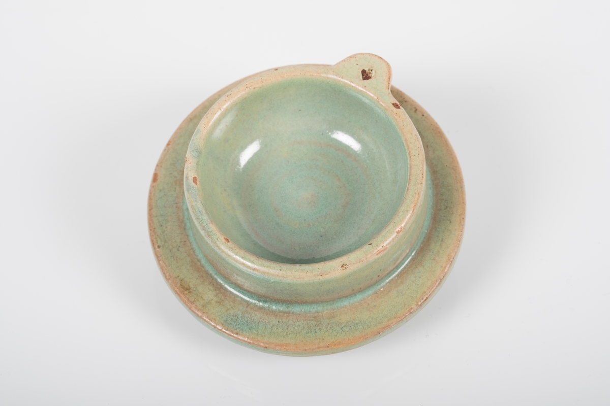 Lokk til tekanne i keramikk med grønn lasur.
Lokket har en rund knott som håndtak.
En liten kant på innsiden av lokket for å holde lokket på plass i kannen.