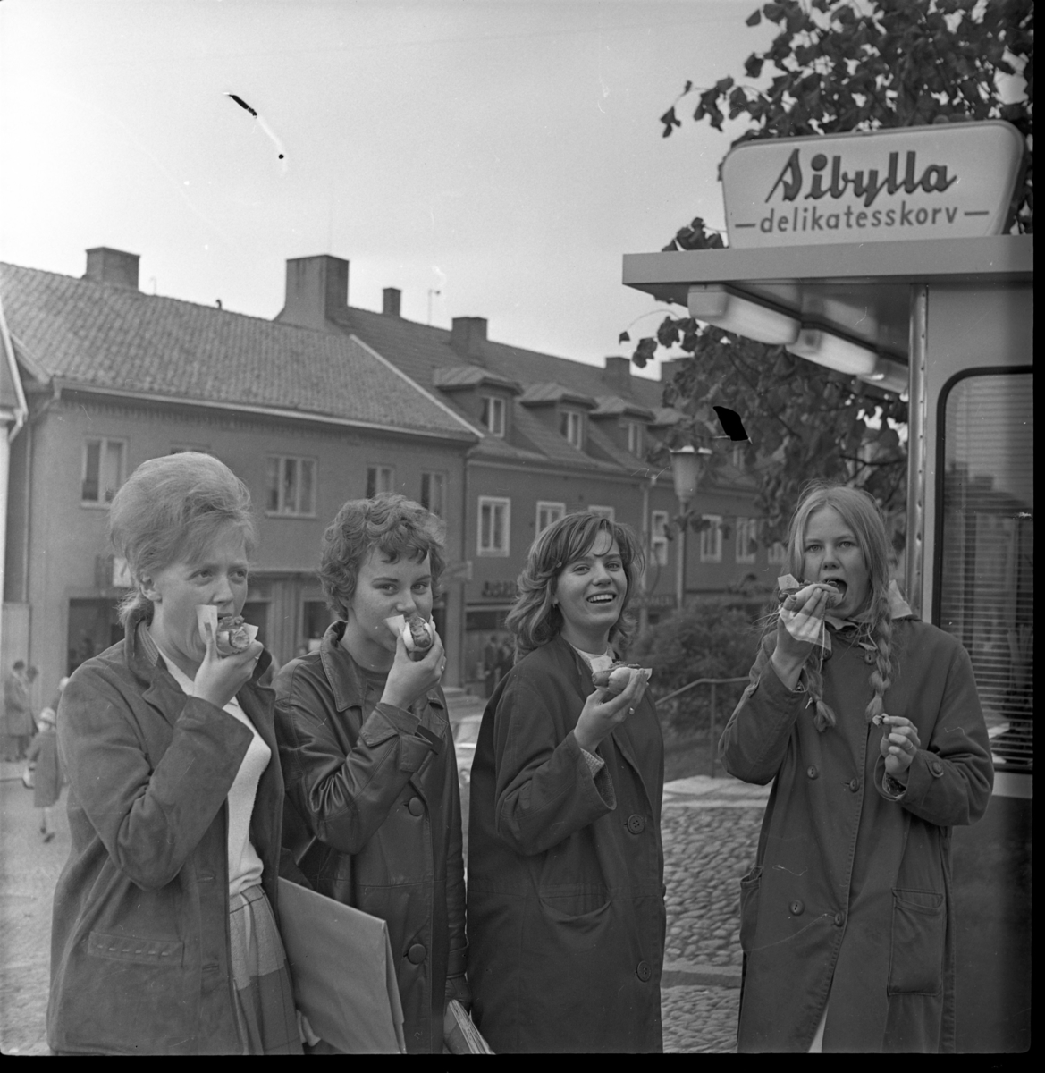 Fyra tjejer äter varmkorv vid Eva Fongs korvkios vid norra uppfarten till Gränna torg. Troligen i samband med en marknad på Gränna torg. Från v: Marianne Martini, Marianne Andersson, Birgitta Karlsson, Marita Wallmo samt Siw Rendahl.