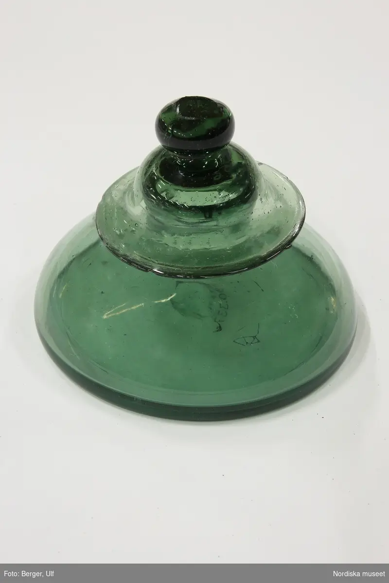 Huvudliggaren:
"Bläckhorn av grönt glas, med lock (en bit slagen ur kanten), rund, lågt."

Bitar limmade vid kanten på locket.