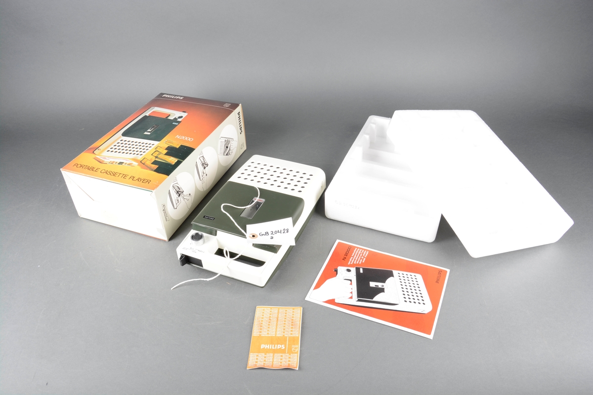 Bærbar kassettspiller brukt i forbindelse med formidling på Bryggens museum. Rektangulær spiller med håndtak på den ene kortsiden. Kassettspilleren har tilhørende bruksanvisning, garantiseddel, eske og isoporemballasje som er tilpasset spilleren.