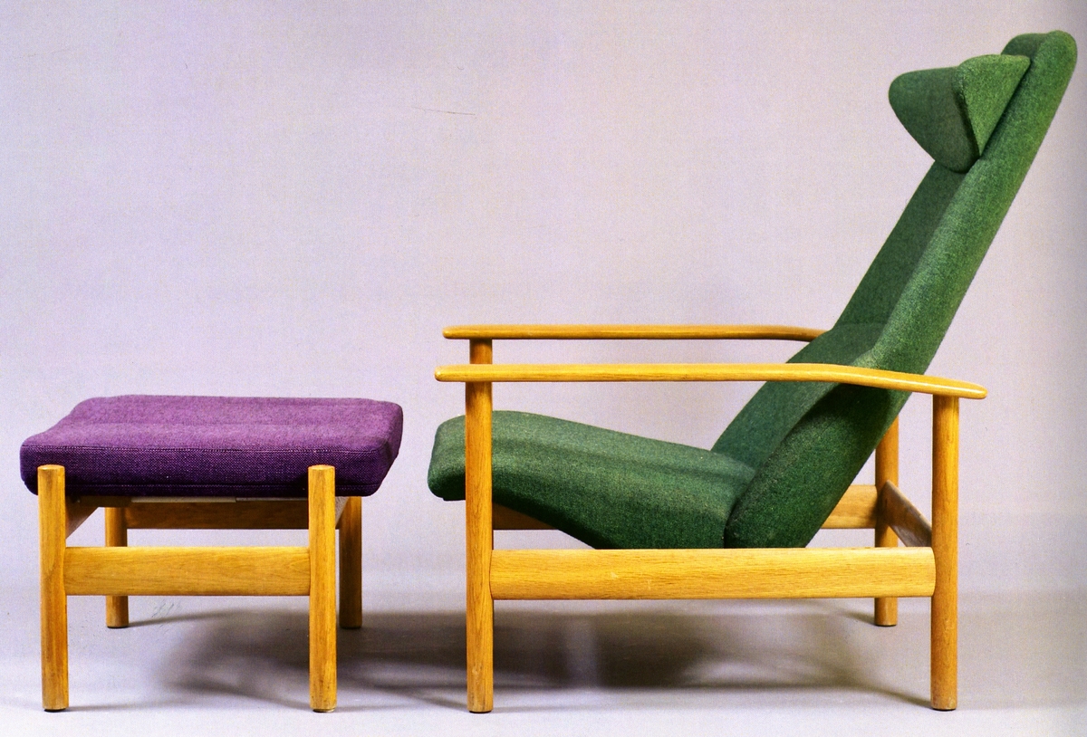 Hvilestol med fotskammel utført i eik og ullstoff. Stolen er trukket i grønn tekstil. Skammel er i lilla tekstil.