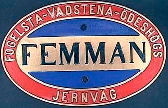 Oval loknamnskylt av mässing med blåmålat mittfält och röd ram.
Lok nr 5, "Femman" från Fogelsta-Vadstena-Ödeshögs Järnväg.