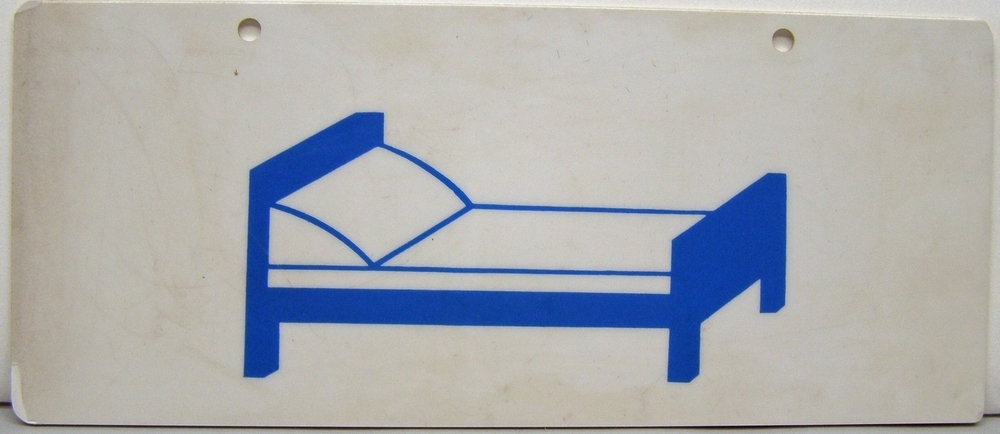 Rektangulär skylt av plast med pictogram i blått på vit botten. Pictogrammet föreställer en stiliserad säng.
Från sovvagn.

Anmärkning: Se även Jvm 15327, 15328, 19629.