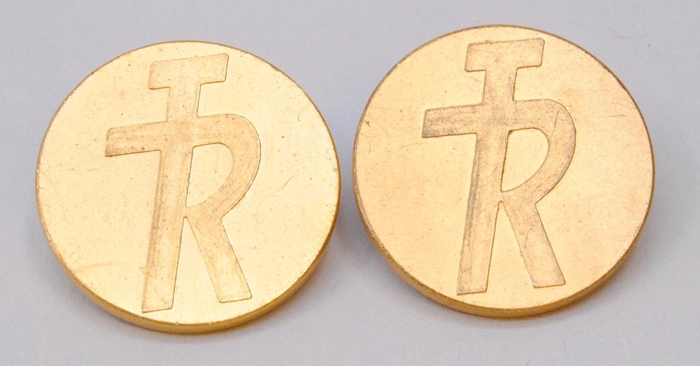 Knapp av guldfärgad metall med TR:s logotyp med bokstäverna "TR" sammanlänkade i relief i form av logotypen "TR-pojken". På baksidan av knappen står det "* C.C. SPORRONG & CO. * STOCKHOLM". 

Se även Jvm15380.