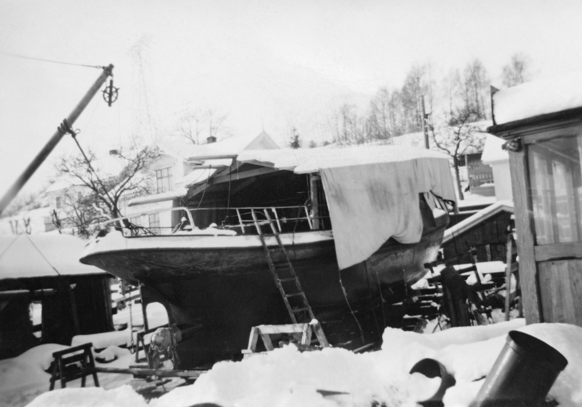 Slepebåten «Axel», som tilhørte Skiensvassdragets Fellesfløtningsforening, fotografert på Knardalstrand slipp og verft i Porsgrunn vinteren 1953-54, da fartøyet ble ombygd fra damp- til dieseldrift.  Her ser vi båten i en fase da man hadde demontert styrhuset, åpnet dekket, for å få ut dampmaskinen ogdiselmotoren inn.  Derfor er den sentrale delen av dekket overbygd med et presenningtelt, som skulle hindre at det kom snø og annen fukt ned i båten.  Dieselmotoren tok atskillig mindre plass enn dampmaskinen hadde gjort.  Dette muliggjorde også betydelige ombyggingsarbeider under dekk, hvor det ble mer lugarplass og mer tidsmessige innredninger.  Styrhuset (til høyre i bildet) ble imidlertid heist på plass igjen og gjenbrukt. 