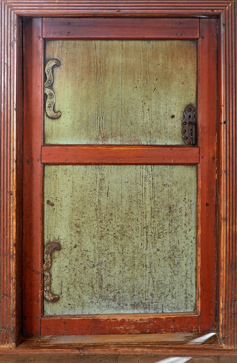 Døra mellom stuerommet og sovekammerset i «Austmostua» eller «Østmostua» på Glomdalsmuseet i Elverum.  Denne bygningen er egentlig fra Mogrenda på Vestsida i Hoff i Solør, men den ble demontert og gjenreist på museet i 1919.  Dette er ei fyllingsdør med to såkalte speil.  De horisontale rammetrærne er tappet inn i de vertikale, og forbindelsene mellom dem er låst med trenagler.  Disse komponentene er innsatt med rødbrun maling.  Trespeilene som fyller de to rommene mellom rammetrærne er planhøvlete.  De er innsatt med et tynt grågrønt malingslag, men vi aner likevel årringstrukturen i underliggende ved.  Døra har to hengsler, som later til å være ført gjennom rammetreet mot venstre dørkarm.  Hver hengsle har imidlertid også to S-formete blader som er naglet til hvert sitt dørspeil.  På motsatt side av dørbladet finner vi et låsblikk med et profilert bøylehandtak.  Fotografiet viser også dørterskelen, samt brunmalt belistning med høvlet stripemønster.  Vi vet ikke sikkert om denne døra har fulgt bygningen fra dens tidligste år i Solør, men stilmessig sett harmonerer den godt med bygningskonstruksjonene.  

I 1782 foregikk det en dølgsmålsfødsel på Velstu Austmo, muligens i denne bygningen.  Fotografiet er tatt som illustrasjonsforslag til en artikkel som tar utgangspunkt i denne saken, se fanen «Historikk».