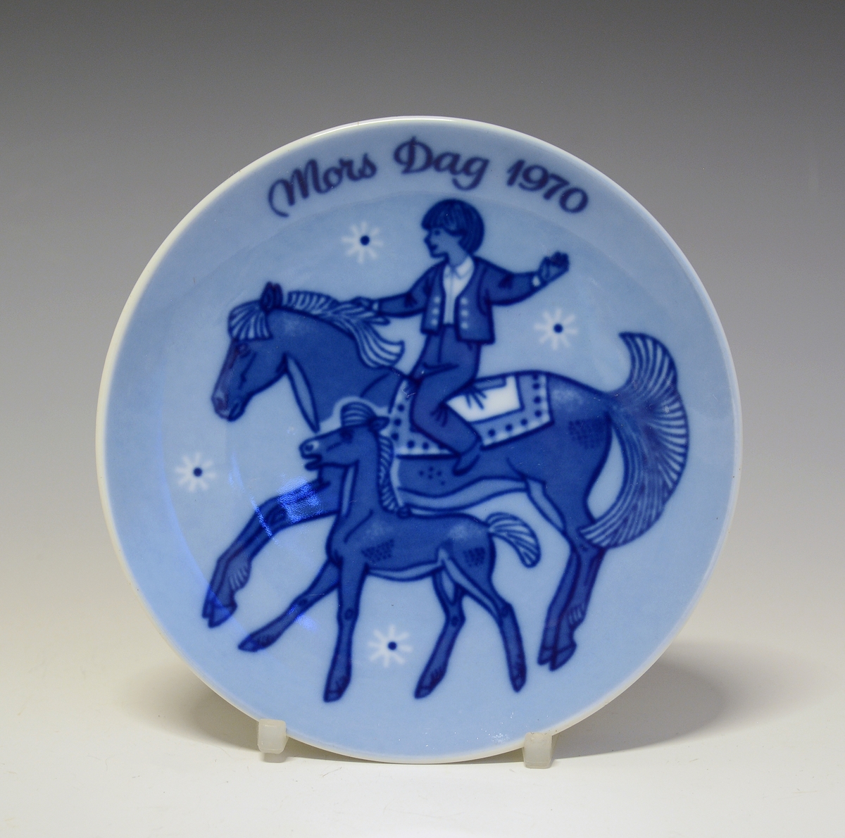 Platte i porselen med blå trykkdekor. Morsdagsplatte med avbildet gutt på hesteryggen, hesten med føll ved fot.