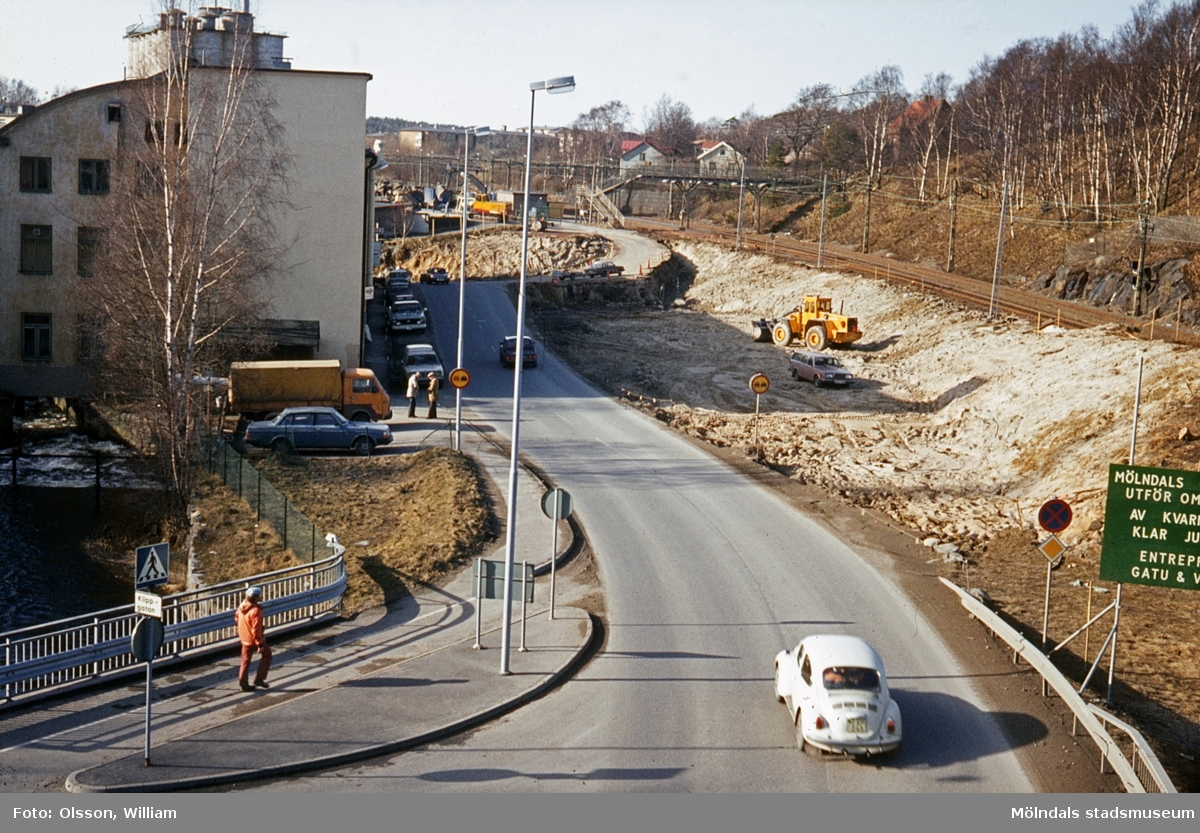Vy från Stensjögatans bro västerut, okänt årtal. En vit Volkswagen "Bubbla" kör Pixbovägen ner. Till vänster ses ett staket och under Rackarebron rinner forsen. Byggnaden är "Strumpan" (Kvarnbygatan 10-14) där bilar står parkerade utanför. Till höger pågår vägarbete för att flytta Kvarnbygatan. Längst bort löper järnvägen Boråsbanan.