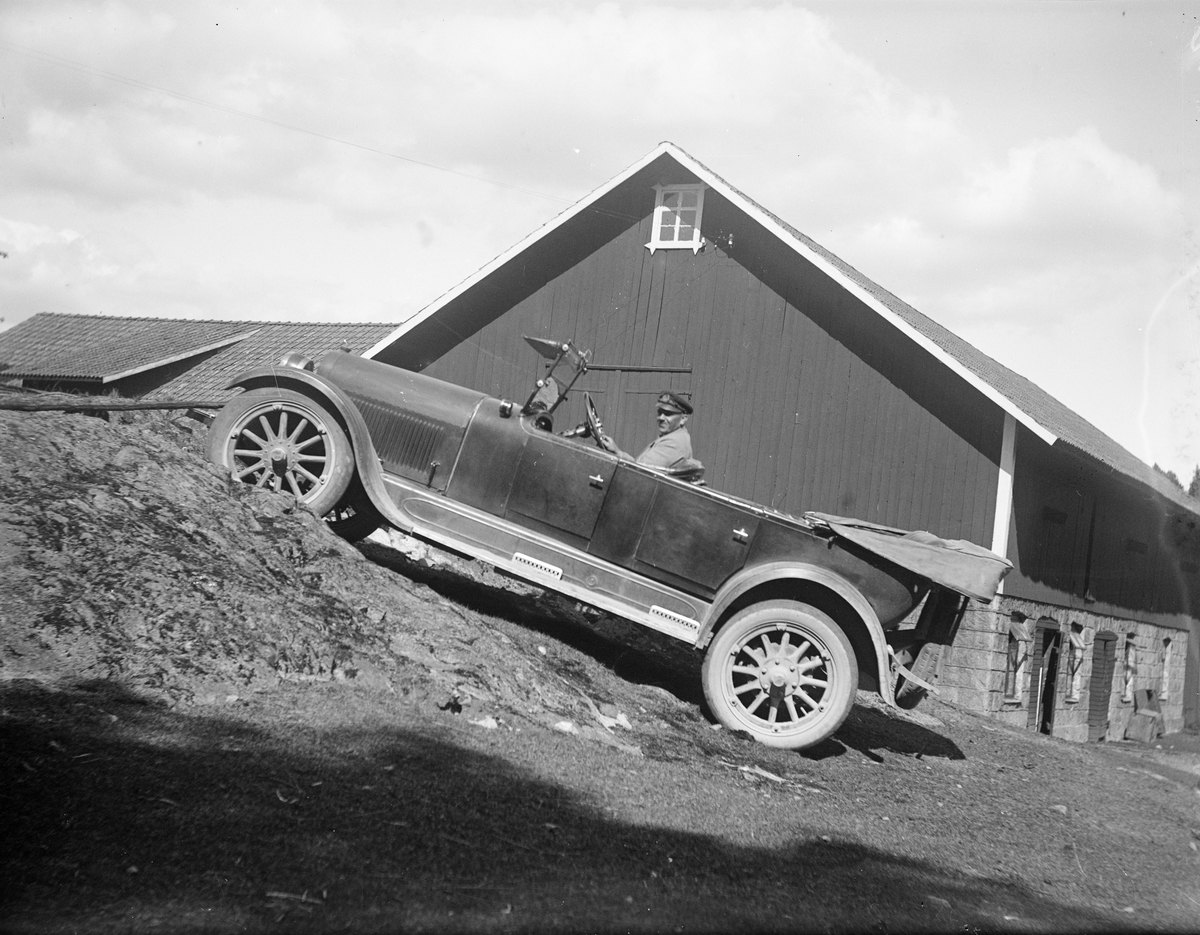 Edvin Sagström kör bil uppför backe vid ladugård, sannolikt Altuna socken, Uppland 1925