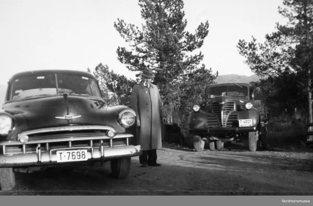 Fra venstre Chevrolet 1949, Fargo 1939 lastebil. (Info fra Ivar Stav),  Lastebilen er en Fargo fra mellom 1939 - 1947, sier Arnfinn Herkedal -Fargo lastebilen er nok en 1946 modell. (mener Jo-Olav Bakken). --- en mann mellom to kjøretøy. Den ene en bil med skilt "T-7698" mens den andre ser ut til å være en leievogn/lastebil med skilt "T-4021". Det er usikkert hvor bildet er tatt, men trolig på Nordmøre i Møre og Romsdal. Fra Paulsen-samlingen, ved Nordmøre museums fotosamlinger.