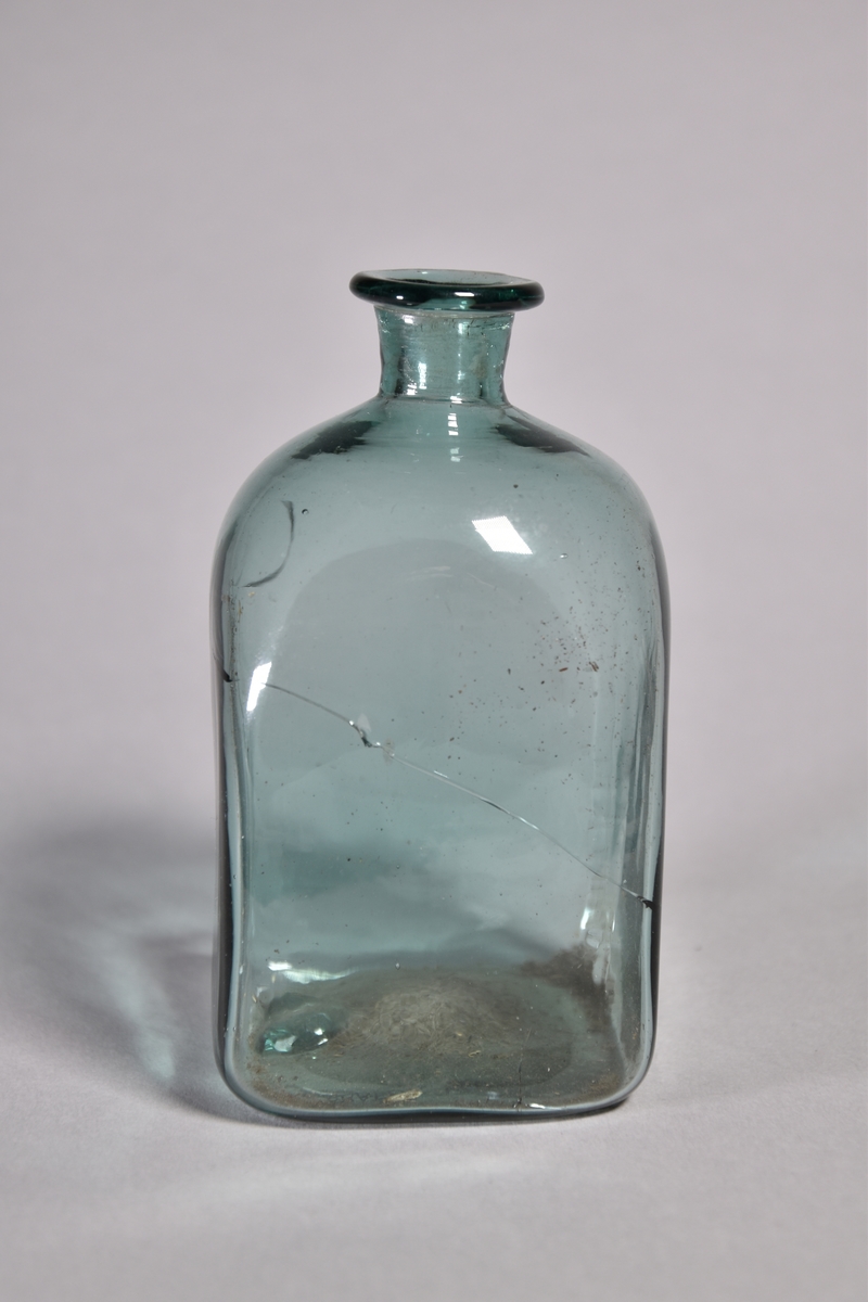 Flaska av grönt glas, kvadratisk, kort hals med utvikt mynning.
Spräckt.