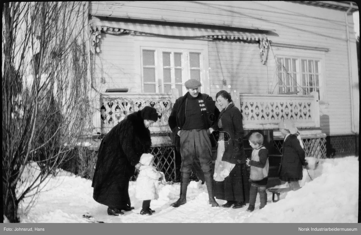 Mann, to kvinner og tre barn stående utenfor bolighus i vinterklær.