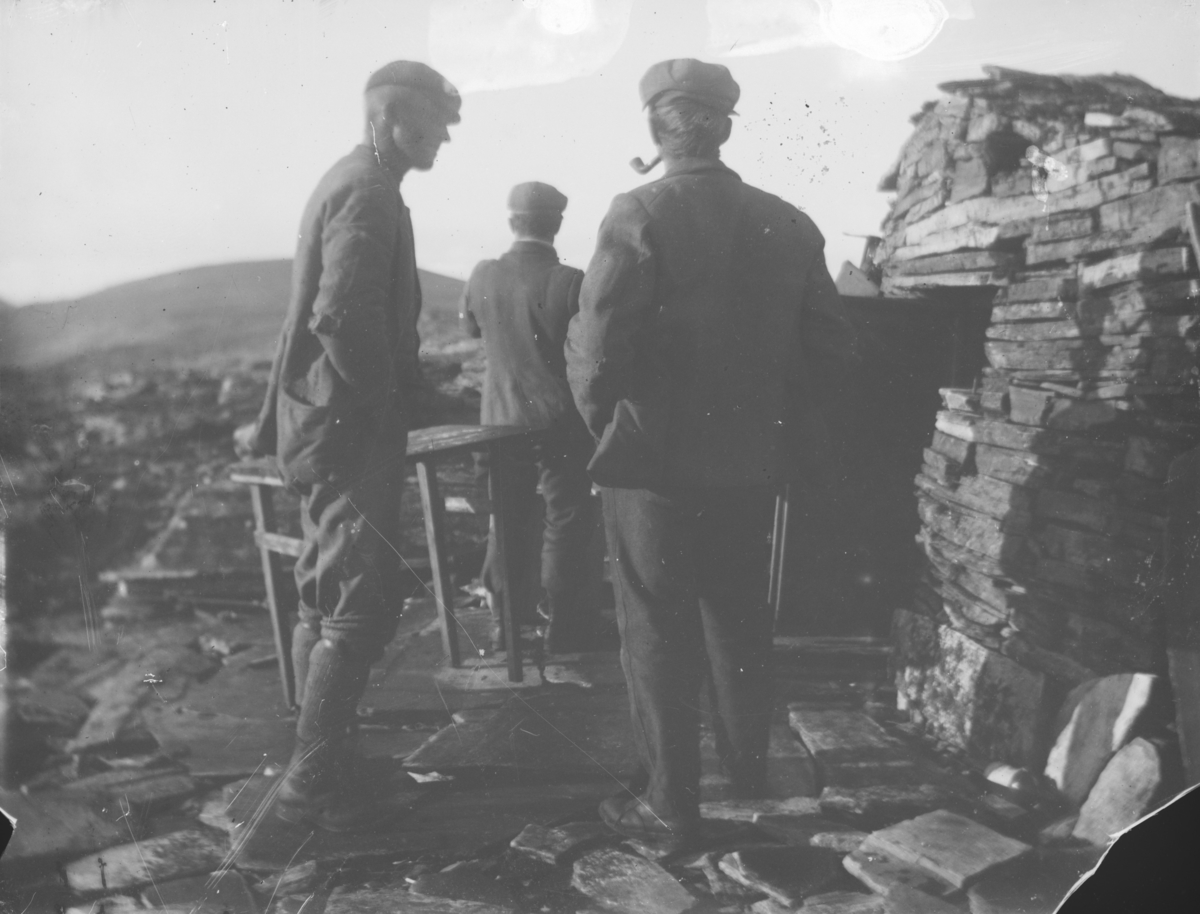 Tre menn ved steinbu på fjellet