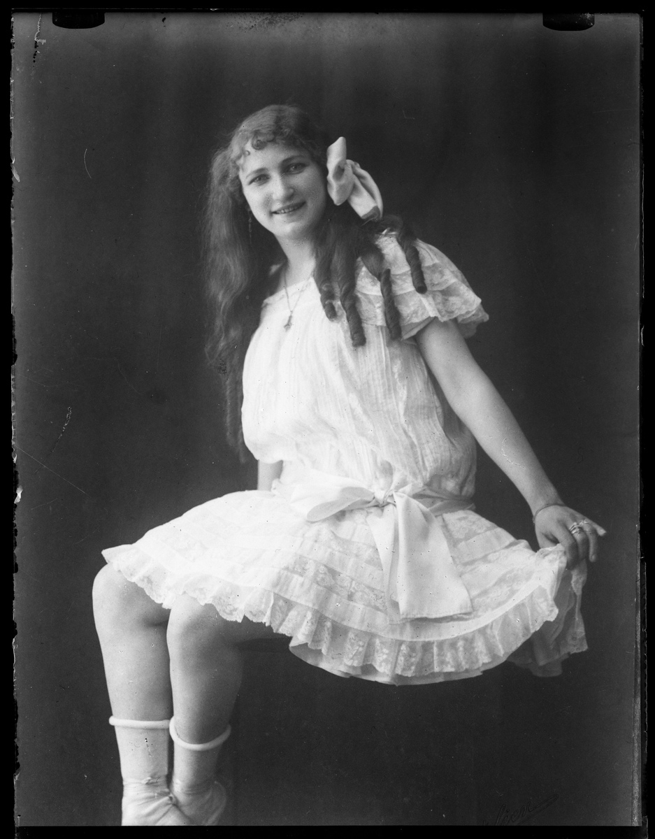 Rosa Wrobello i vit knälång klänning, vita strumpor och vit rosett i håret.