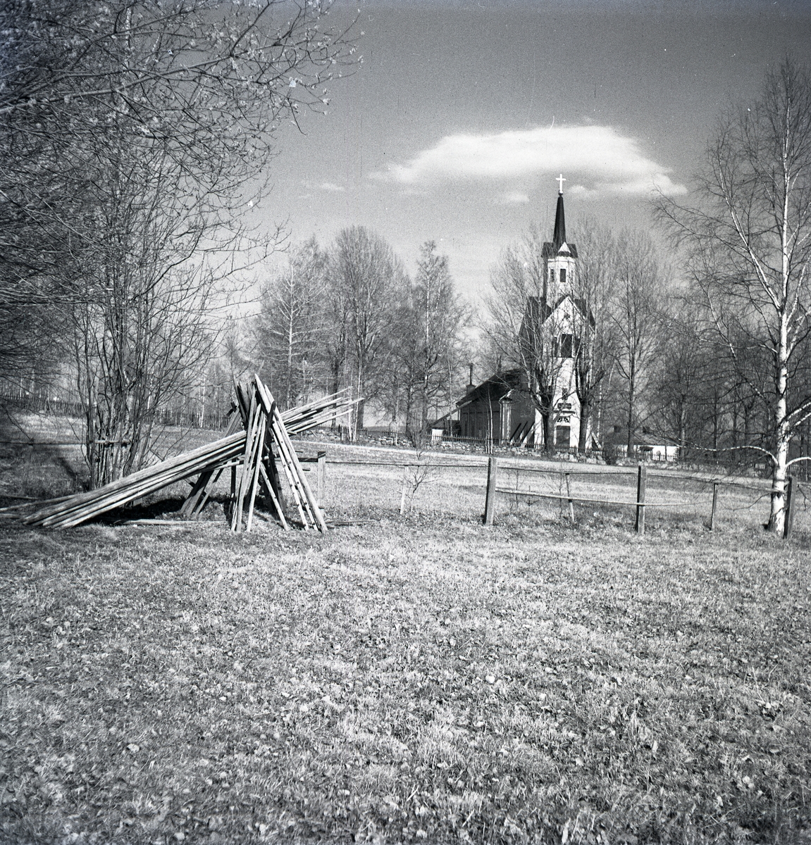 Los kyrka bakom en ställning hässjevirke på ett fält.