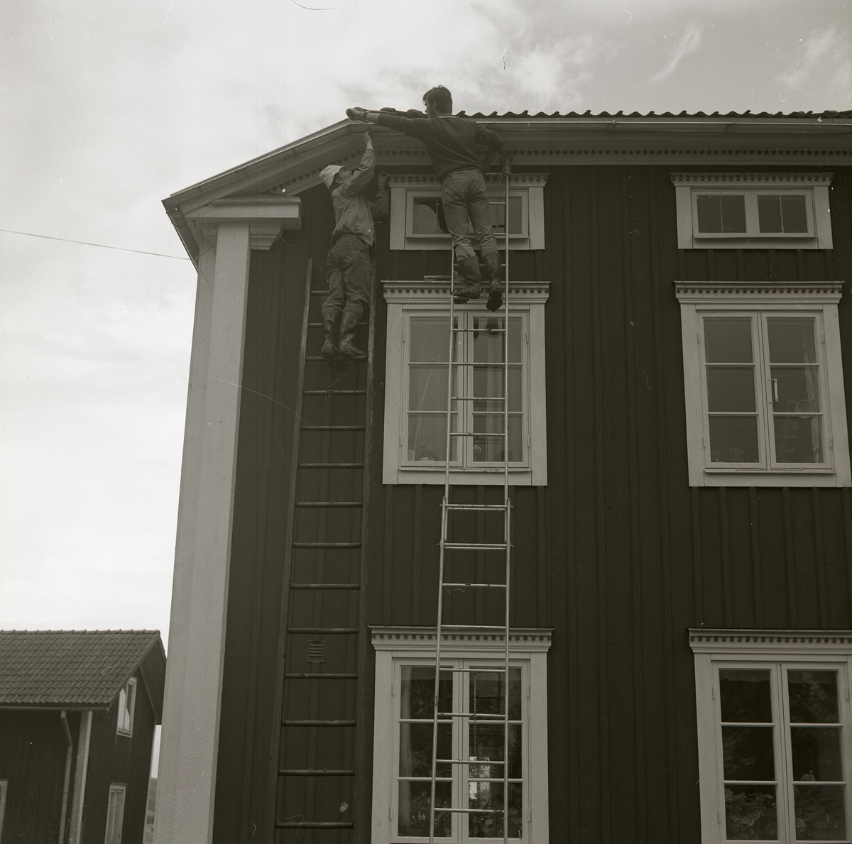 Två män står på var sin stege och arbetar med taket på bostadshuset vid gården Sunnanåker, 1970.