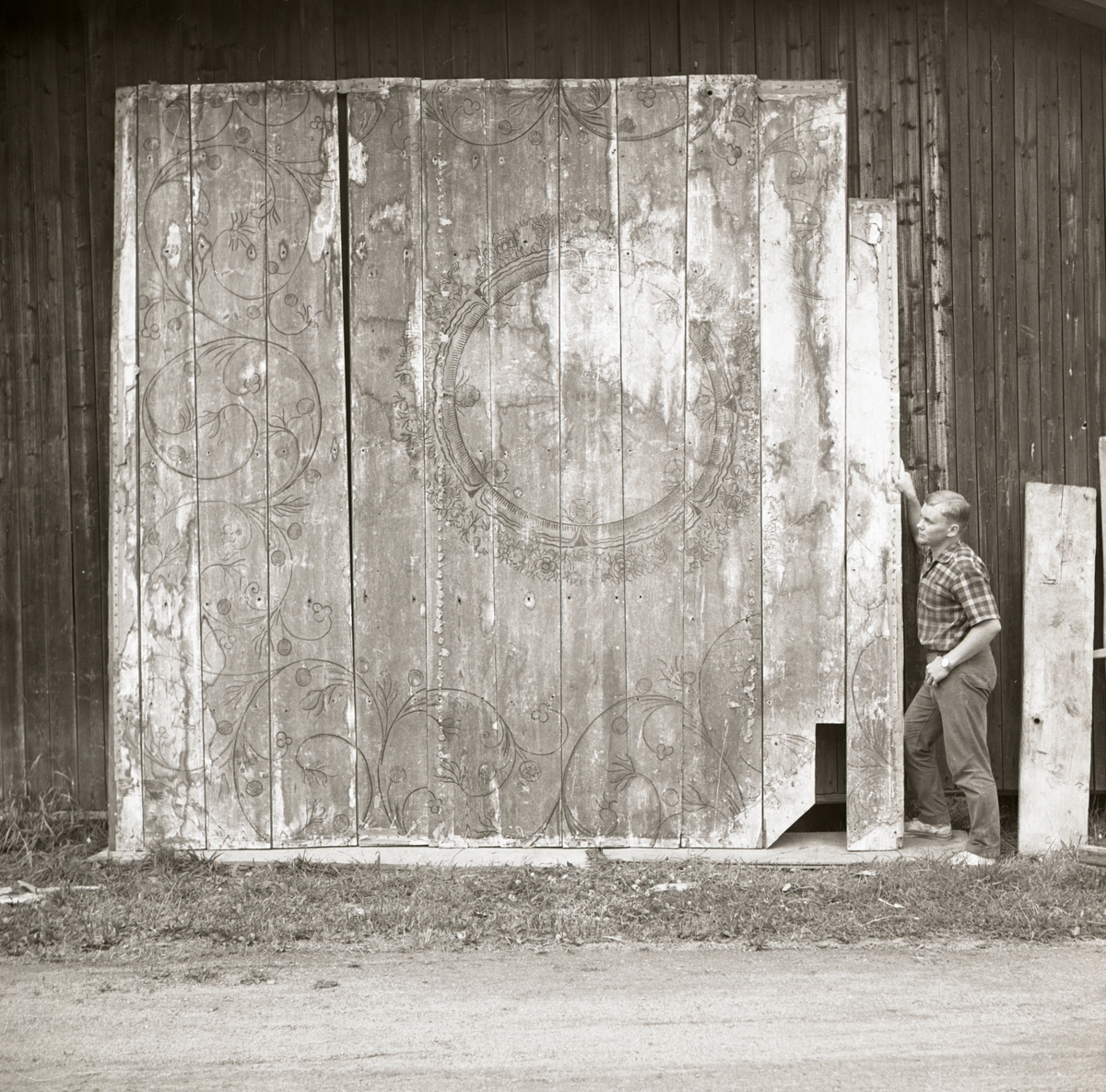 En man står bredvid målade innertaksbrädor vilka är lutade mot en vägg, 1968-1969.