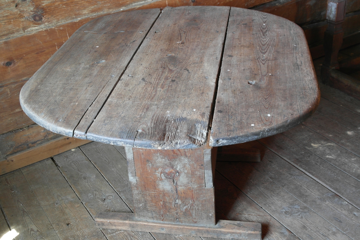 Bord i hugget, høvlet og pusset furu. Bordet har oval bordplate som er satt sammen av tre bord, samt  bukkebein som er avstivet på langs med to brede bord.