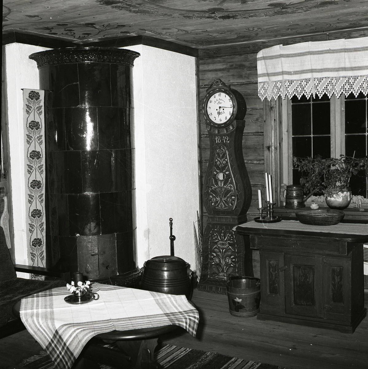 Interiör med takmålning från gården Sunnanåker, 12 juni 1981. Där finns en kakelugn, ett golvur och en skänkskåp i trä.