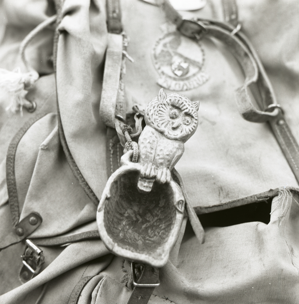En ryggsäck med en uggla samt en kåsa fastsatt i en av remmarna.