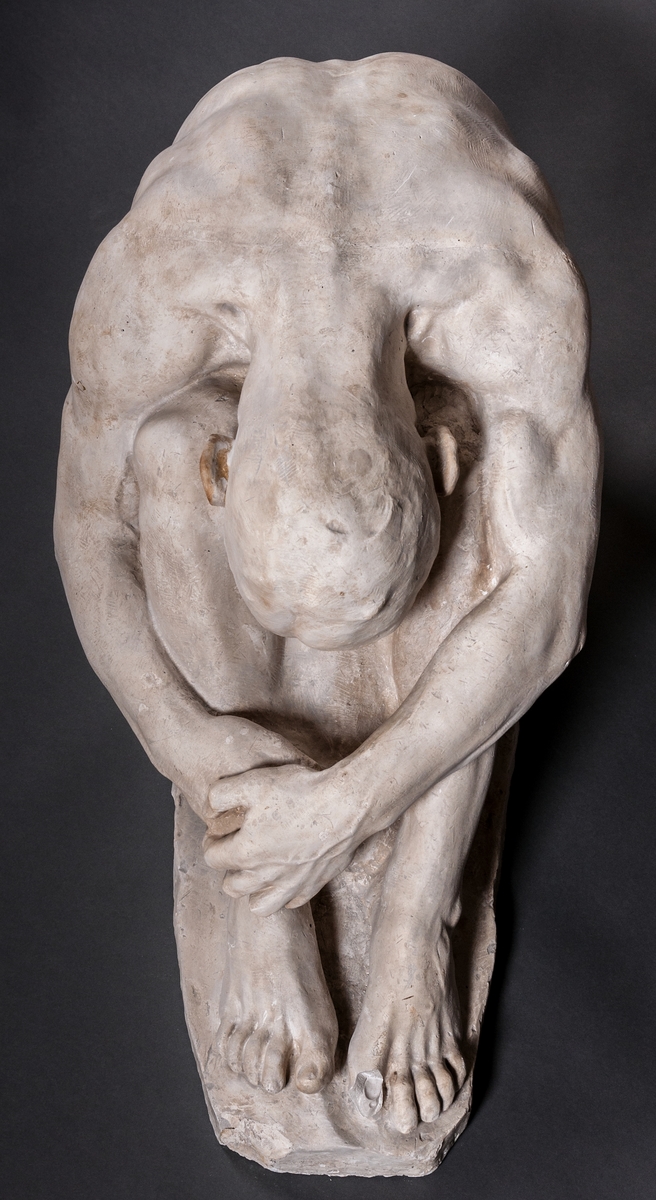 Skulptur i gips, detalj av gravmonument, kallad "Sorg", av John Runer. Återger en man naken sittande på marken, med huvudet ner mellan knäna.